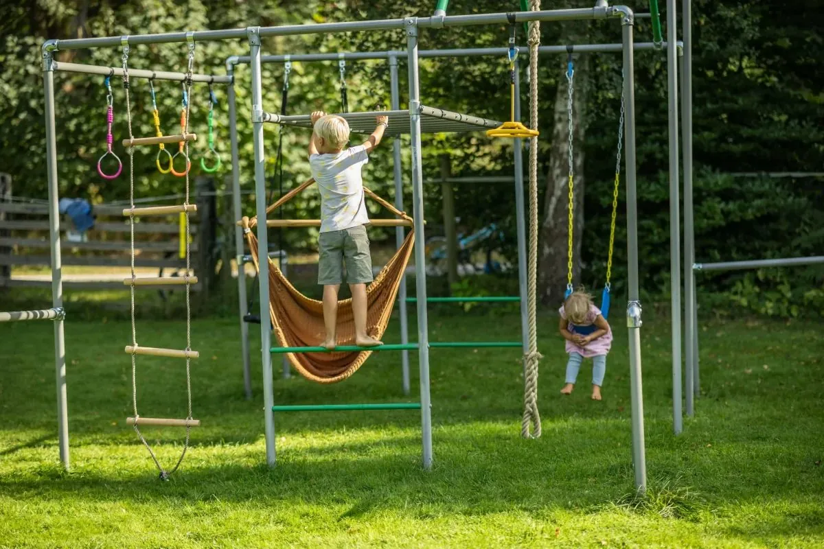 Kinder spielen frei am Klettergerüst: eines liegt in der Hängematte, eines steht an der Leiter