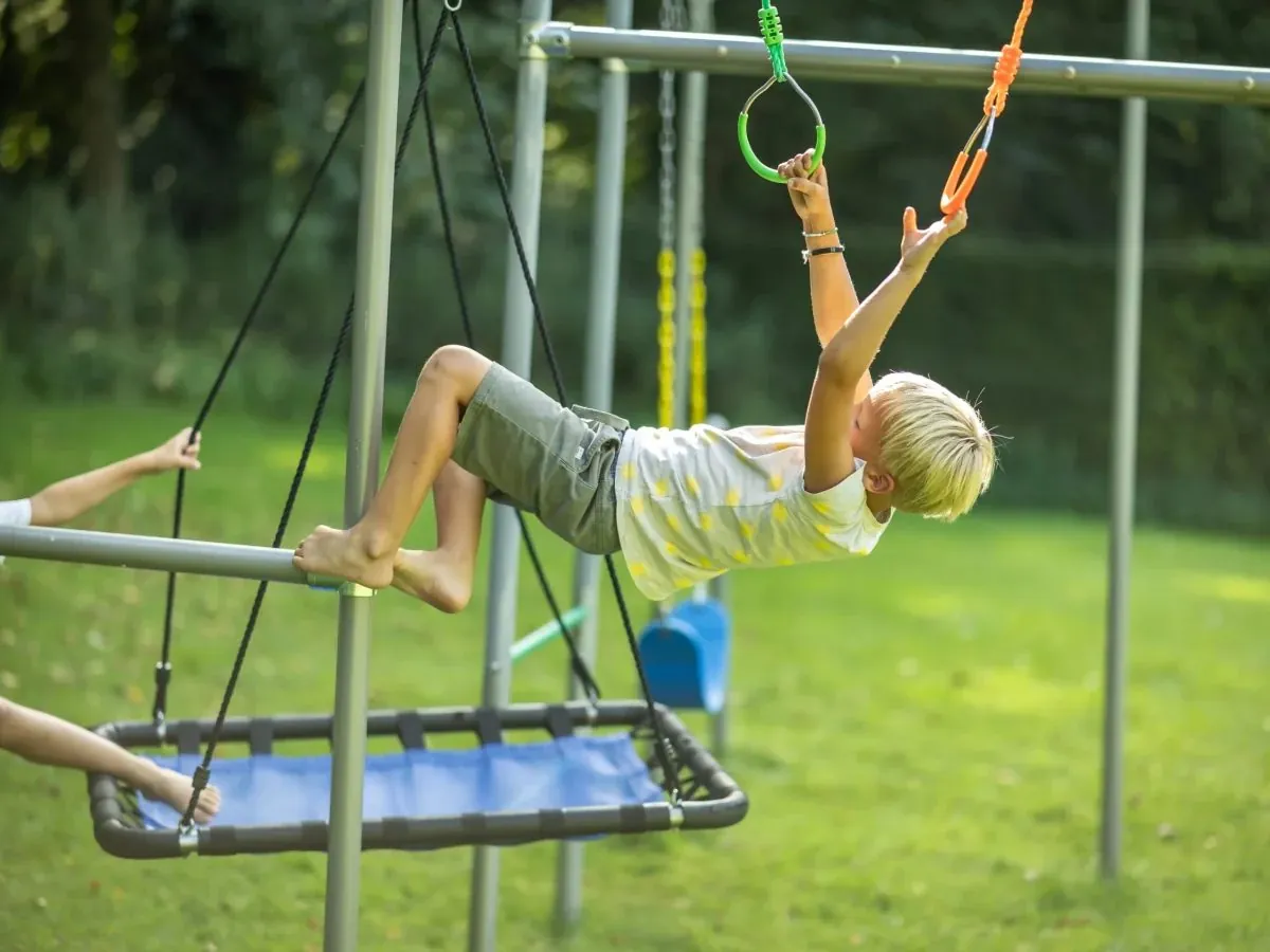 Junge hangelt sich an Turnringen über die Platform Swing, ohne den Boden zu berühren