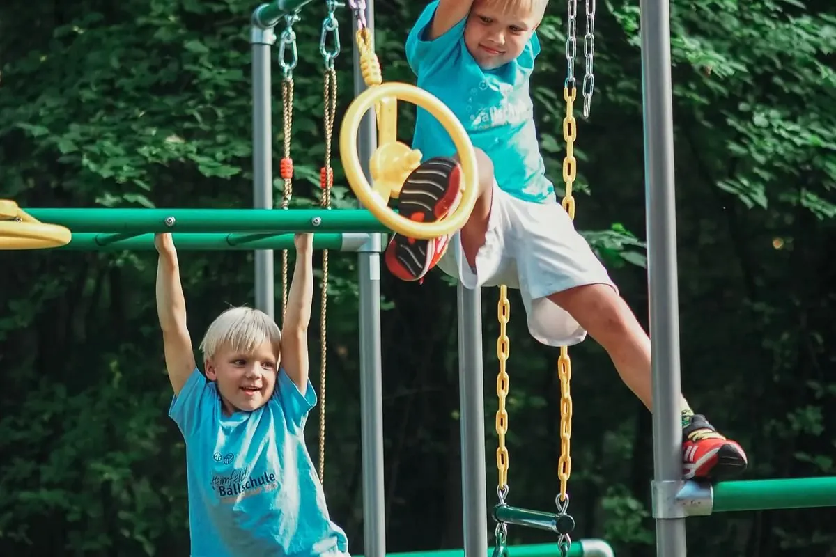 Zwei Jungen hangeln am Ninja Wheel und an Turnringen eines grünen Klettergerüsts