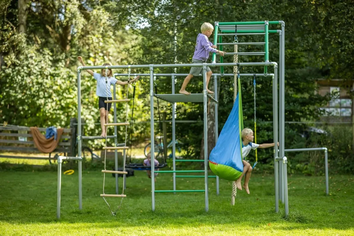 Kind oben auf einem Klettergerüst im Garten, darunter Hängesessel und Strickleiter