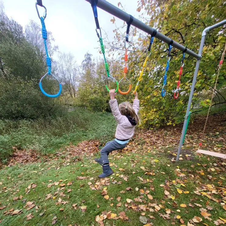 Mädchen hangelt an bunten Turnringen über Herbstlaub