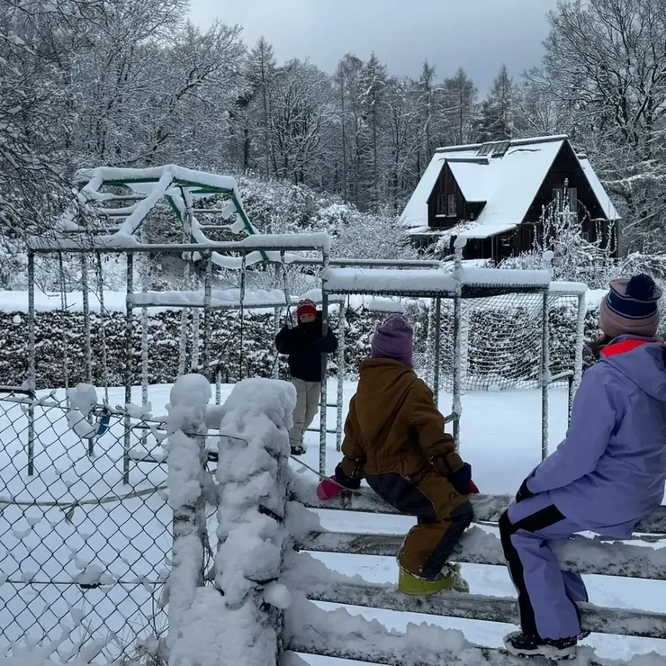 Kinder sitzen im Schnee vor einem verschneiten Klettergerüst