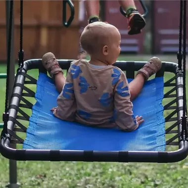 Kleinkind sitzt auf der blauen Platform Swing am Klettergerüst