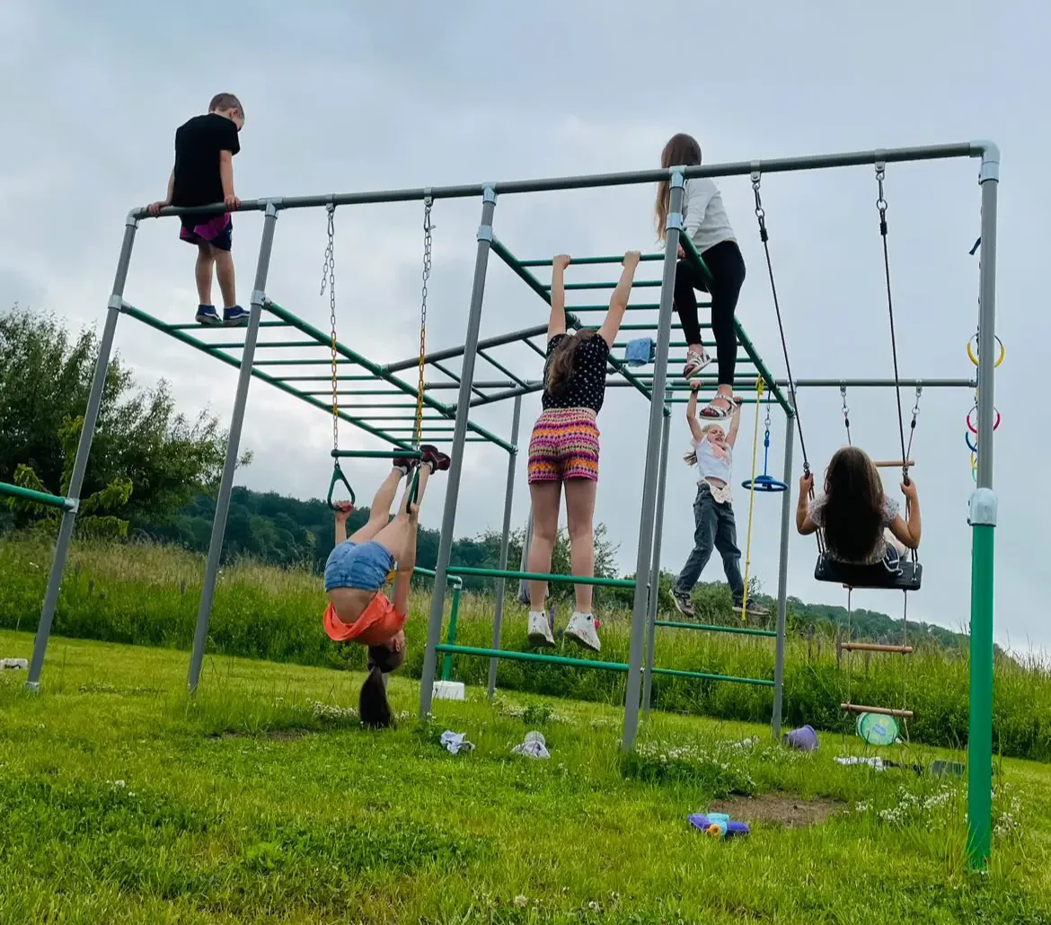 Fünf Kinder klettern, hangeln und schaukeln gleichzeitig an einem großen Klettergerüst