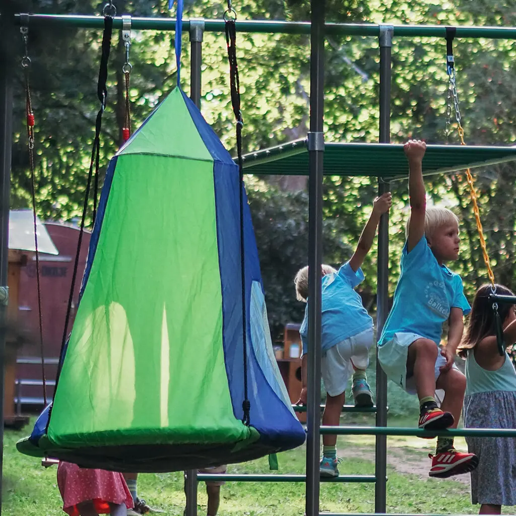 Canopy Swing Nestschaukel mit Sonnendach am Klettergerüst, Kinder klettern im Hintergrund