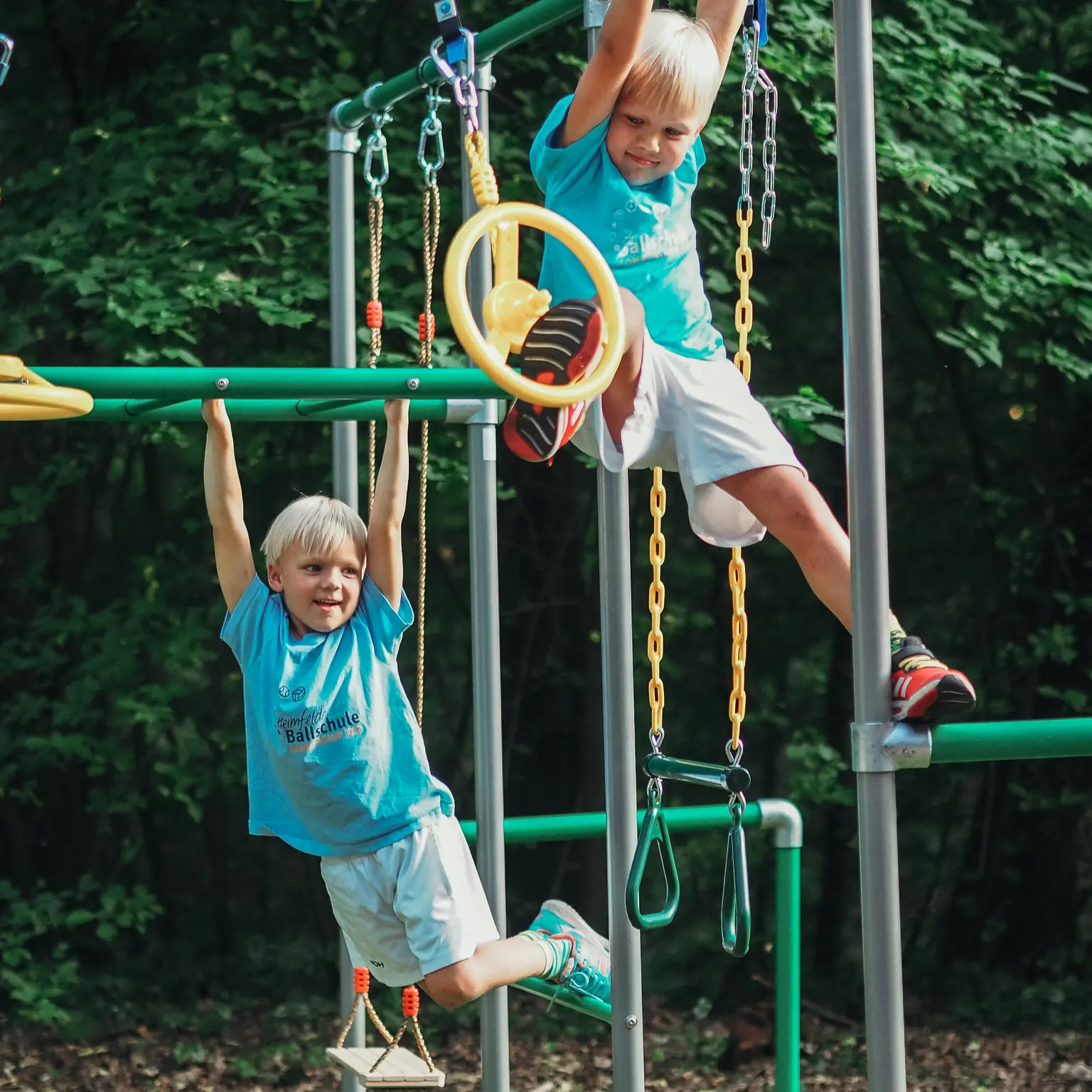Zwei Kinder spielen gleichzeitig an einem FOURACTION-Klettergerüst: eines hängt an einer Stange, eines schwingt sich an einem Ninja Wheel