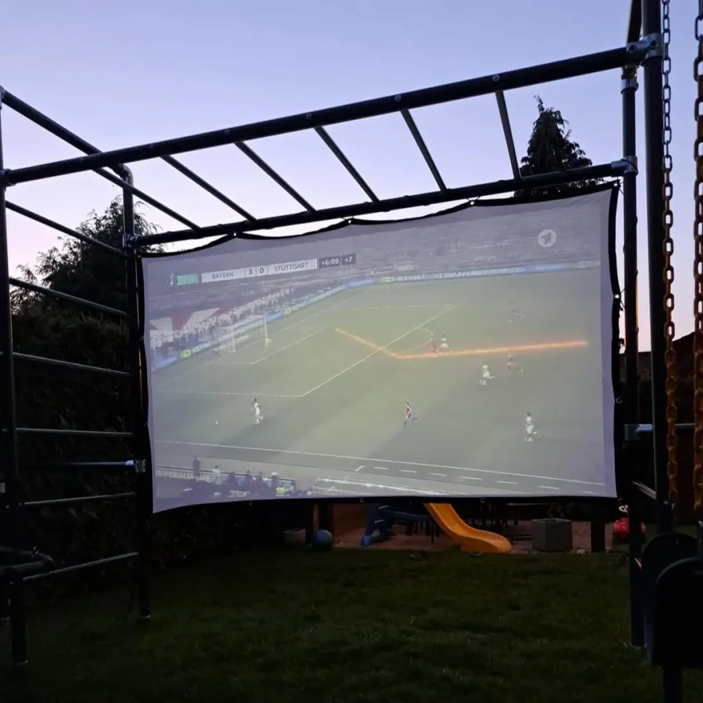 Outdoor-Leinwand am Klettergerüst bei Dämmerung zeigt Fußballspiel