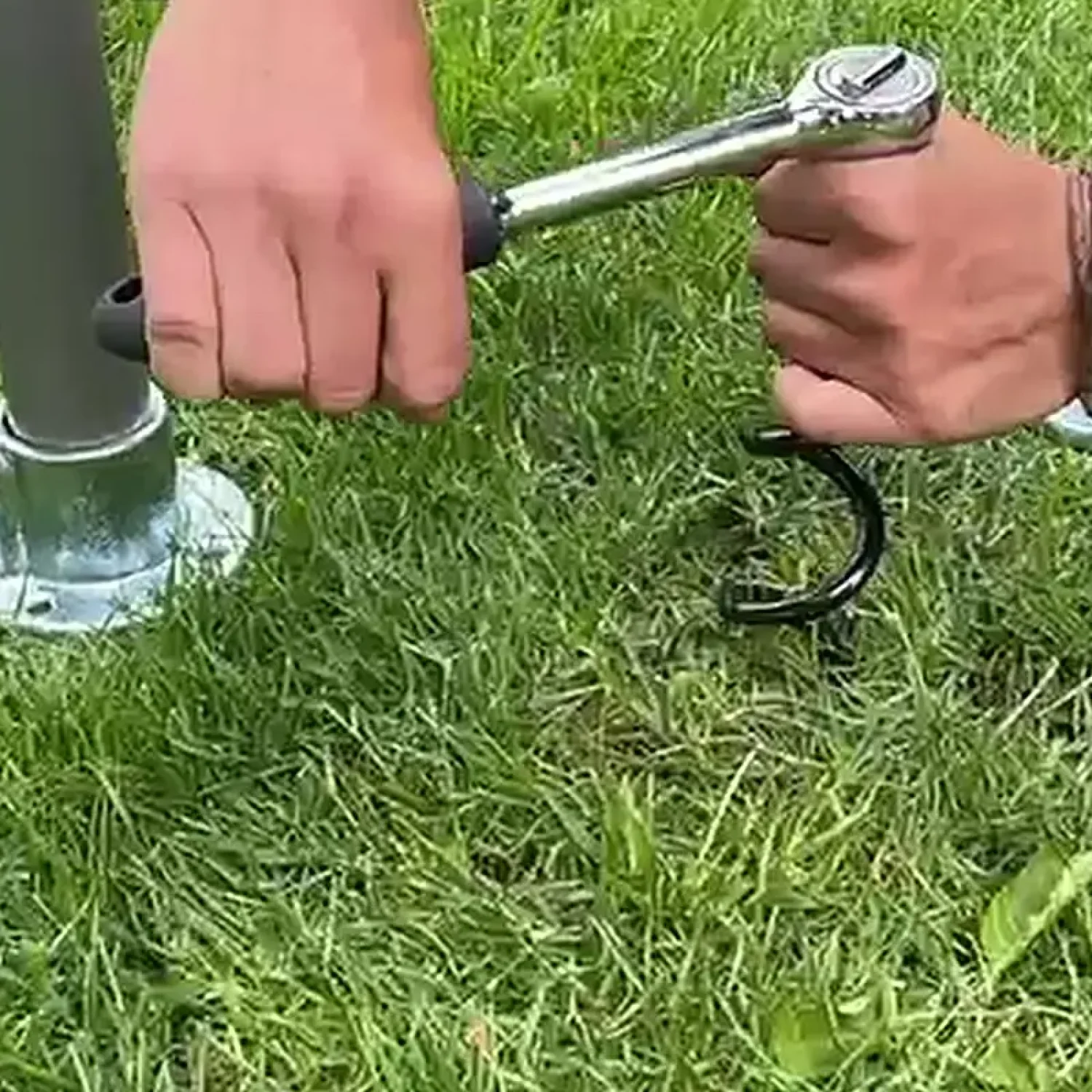 Klettergerüst Spiralhering eindrehen mit Ratsche – Bodenverankerung ohne Beton | FOURACTION Person dreht FOURACTION Spiralhering mit Ratsche in Gartenrasen – Klettergerüst Bodenverankerung ohne Beton, mit Boden-Rohrverbinder und Bodenplatte sichtbar